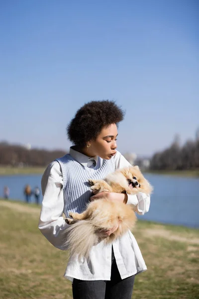 Curly african american woman sending air kiss to pomeranian dog — Stock Photo