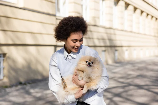 Cheerful african american woman holding pomeranian dog on street — Photo de stock