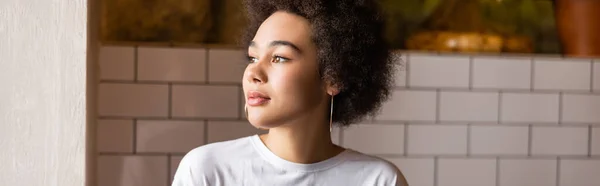 Femme afro-américaine en boucles d'oreilles cerceau et t-shirt blanc détournant les yeux, bannière — Photo de stock