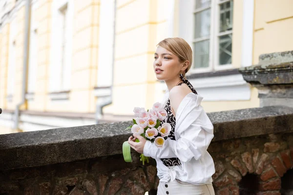 Молода і модна жінка з букетом тюльпанів біля кам'яного паркану на міській вулиці — стокове фото