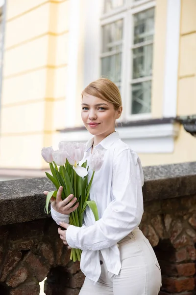 Positive young woman holding white tulips and smiling outdoors — Stock Photo