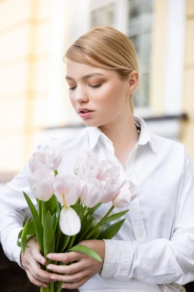 Mulher encantadora em camisa branca segurando flores frescas ao ar livre — Fotografia de Stock