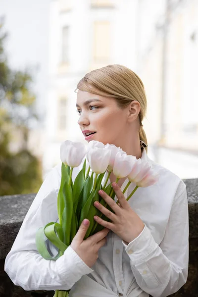 Bella donna guardando lontano, mentre tenendo tulipani bianchi all'aperto — Foto stock