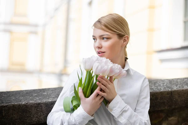 Donna bionda con bouquet di tulipani bianchi che guardano all'aperto — Foto stock