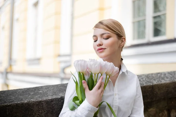 Femme blonde souriante tenant bouquet de tulipes blanches sur la rue de la ville — Photo de stock