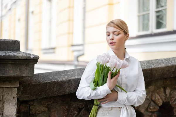 Femme en chemise blanche debout avec bouquet de tulipes près d'une clôture en pierre — Photo de stock
