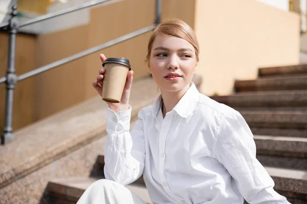 Молода жінка в білій сорочці тримає паперову чашку і дивиться геть — Stock Photo