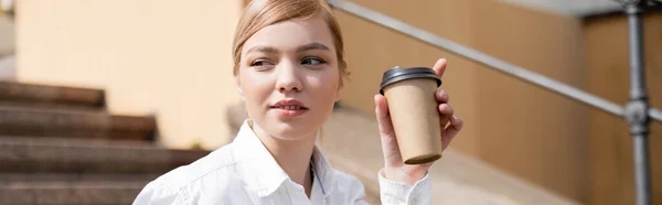 Joven rubia con bebida para llevar mirando al aire libre, pancarta - foto de stock