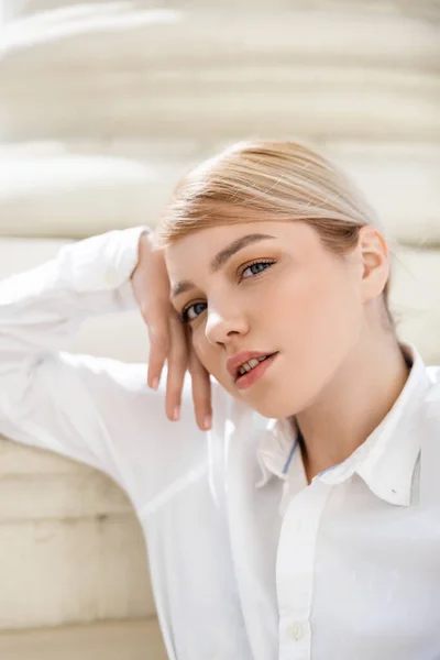 Charming blonde woman with hand near face looking at camera outdoors — Stock Photo