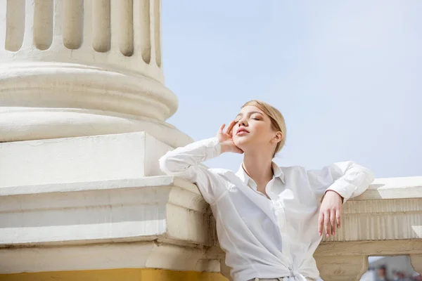 Young woman with closed eyes touching face while standing near column — Stock Photo