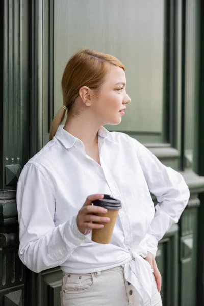 Femme blonde avec à emporter boisson regardant loin près du mur gris — Photo de stock