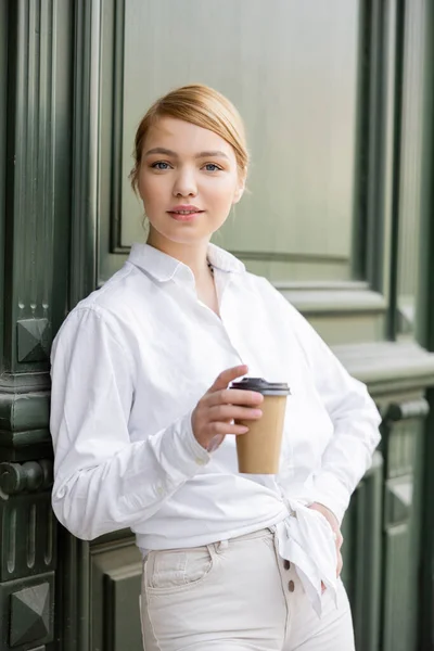 Giovane donna in t-shirt bianca in piedi con mano sul fianco vicino muro grigio — Foto stock