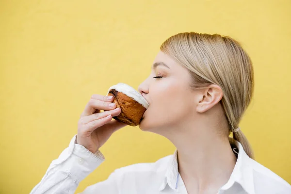 Blondine isst leckeren Cupcake isoliert auf gelb — Stockfoto