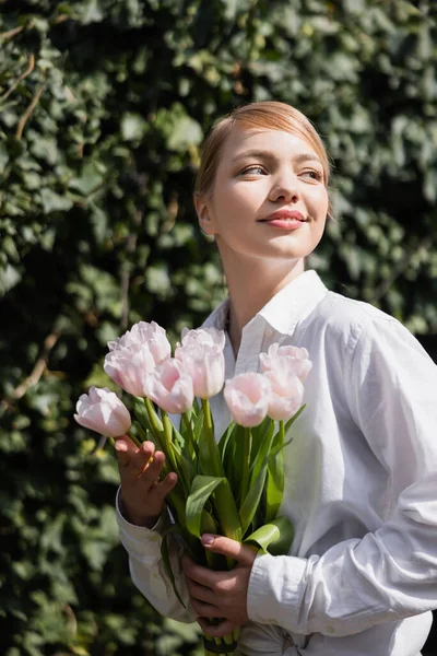 Mulher sorridente com tulipas brancas frescas olhando para o exterior — Fotografia de Stock