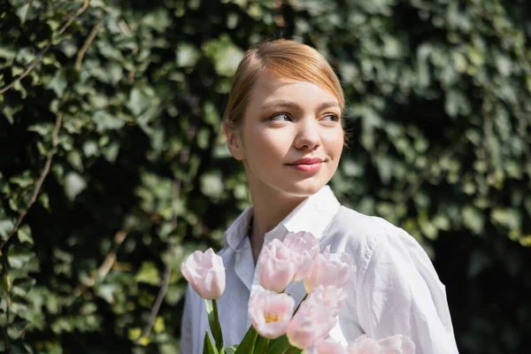 Fröhliche Frau mit Strauß weißer Tulpen, die draußen lächelt — Stockfoto