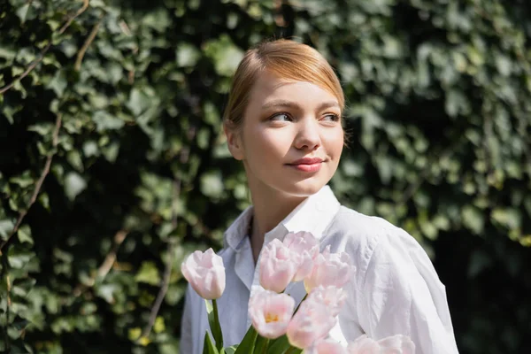 Cheerful woman with bouquet of white tulips smiling outdoors — стоковое фото