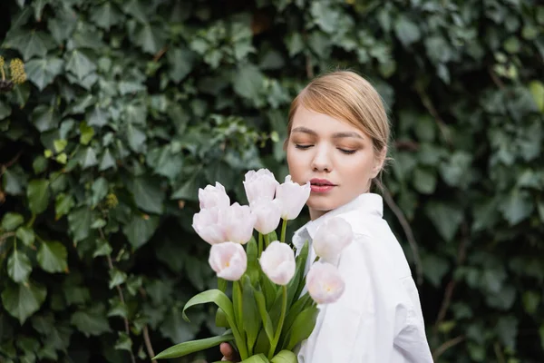 Charmante femme avec bouquet de tulipes blanches debout près de lierre vert — Photo de stock