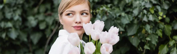Pretty young woman with tulips looking away outdoors, banner — Stock Photo