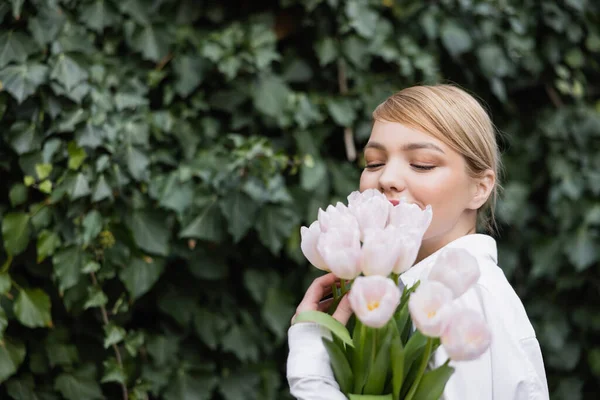 Feliz jovem mulher obscurecendo rosto com tulipas brancas perto de hera verde — Fotografia de Stock