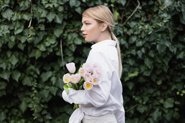 Side view of young woman with white tulips near green ivy outdoors — Stock Photo