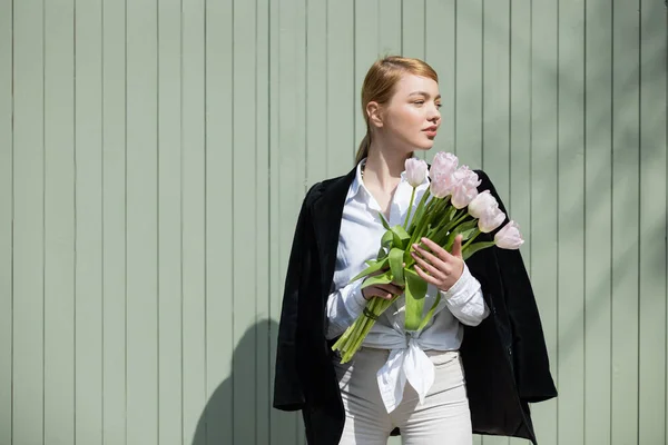 Junge Frau in weißem Hemd und leerem Blazer steht mit Tulpen an grauer Wand — Stockfoto
