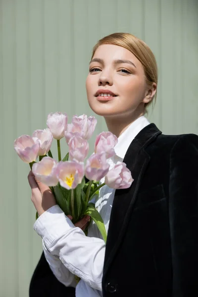 Pleased young woman with bouquet of tulips looking at camera outdoors — Stock Photo