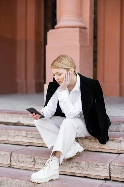 Vista completa de la mujer de moda sentada en las escaleras con teléfono móvil - foto de stock