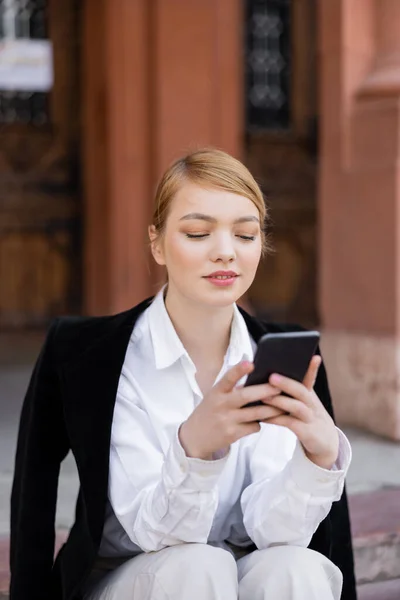 Mujer rubia joven usando el teléfono móvil en la calle urbana - foto de stock