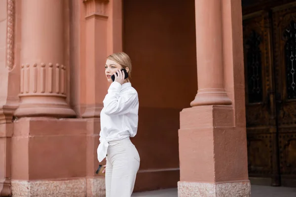 Mulher elegante falando no telefone celular enquanto está perto do edifício com colunas — Fotografia de Stock