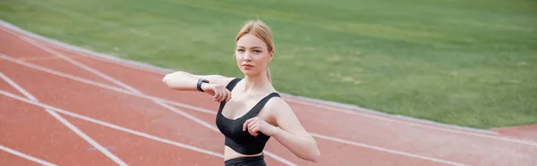 Blonde woman in black sports bra stretching hands on stadium, banner — Stock Photo