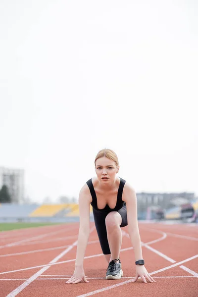 Junge sportliche Frau steht in niedriger Startposition und blickt in die Kamera — Stockfoto