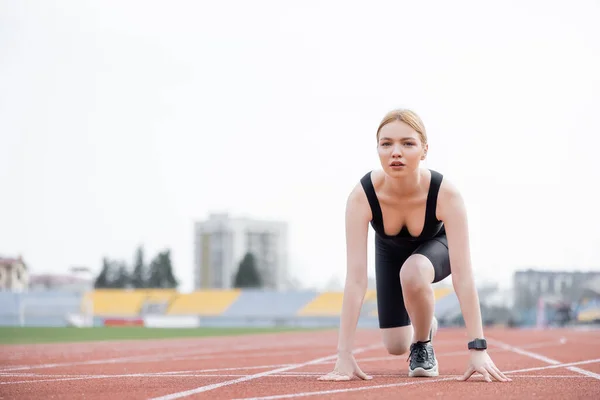 Junge Sportlerin blickt in die Kamera, während sie in niedriger Startposition auf dem Stadion steht — Stockfoto