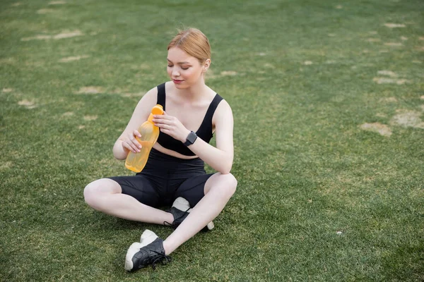 Jeune sportive assise sur le stade et ouvrant une bouteille de sport — Photo de stock
