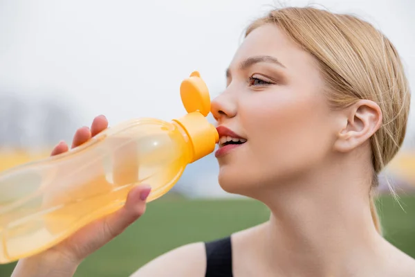 Happy young sportswoman drinking from sports bottle outdoors — стоковое фото