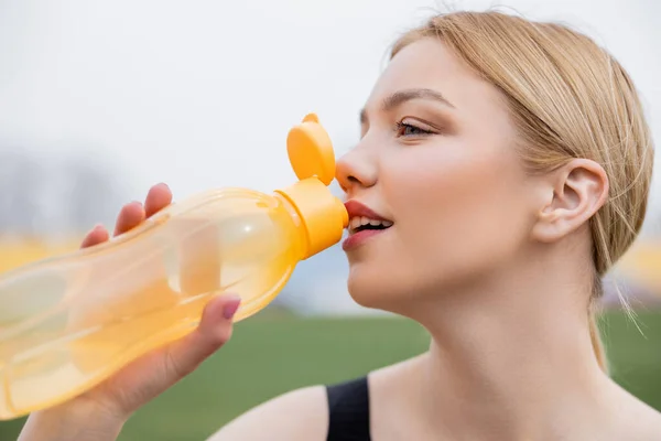 Happy young sportswoman drinking from sports bottle outdoors — Stock Photo