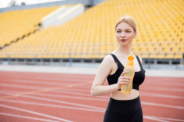 Sportliche Frau schaut weg, während sie Sportflasche im Stadion hält — Stockfoto