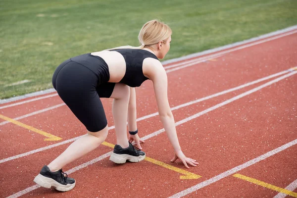 Full length view of woman in black sportswear standing in low start position on stadium — Stock Photo