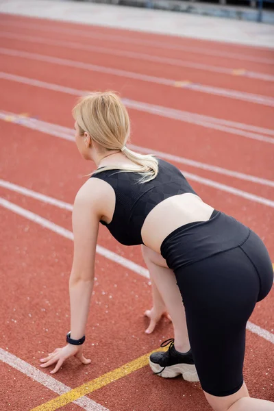 Жінка в чорному спортивному одязі, стоячи в низькому стартовому положенні на стадіоні — стокове фото