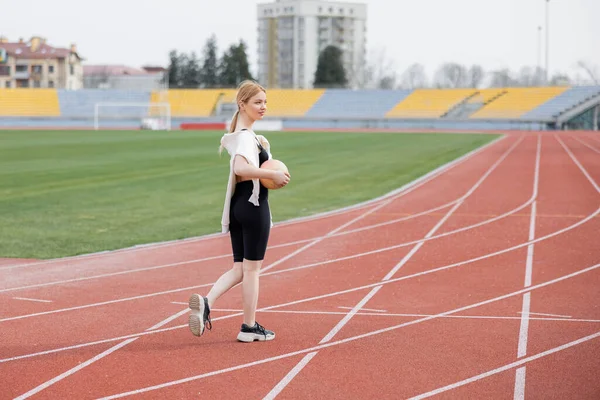 Full length view of sportive woman walking on athletic field with ball — Stock Photo