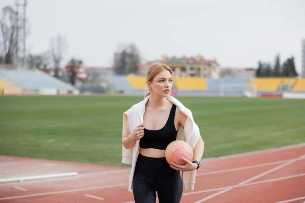 Donna in abbigliamento sportivo nero in piedi sullo stadio con palla e guardando altrove — Foto stock