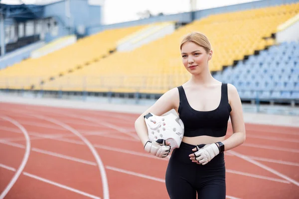 Femme souriante en vêtements de sport tenant casque de sport et détournant les yeux — Photo de stock