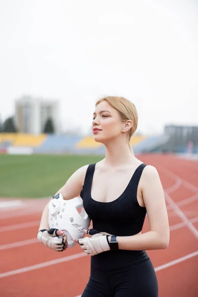 Sportswoman in fitness gloves holding sports helmet and looking away outdoors — стоковое фото