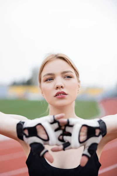 Jeune sportive en gants de fitness regardant loin tout en se réchauffant à l'extérieur — Photo de stock