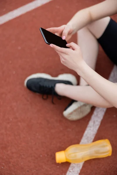 Vista recortada de deportista borrosa sosteniendo teléfono inteligente con pantalla en blanco - foto de stock