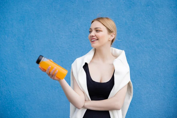 Fröhliche Frau in Sportbekleidung mit Orangensaft auf blau strukturiertem Hintergrund — Stockfoto