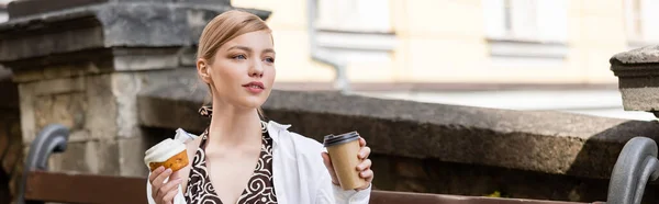 Affascinante donna bionda con drink da asporto e cupcake guardando lontano sulla strada, banner — Foto stock