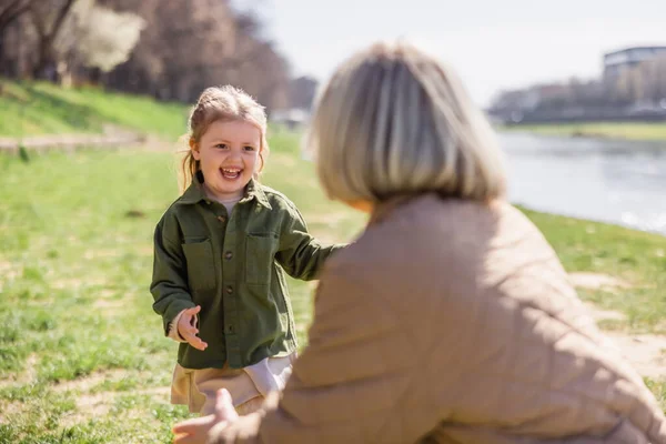 Cheerful girl laughing near blurred mother outdoors — Stock Photo