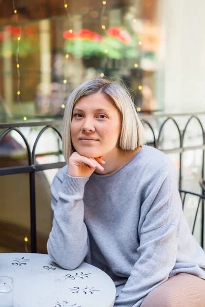 Femme blonde heureuse regardant la caméra tout en étant assis dans le café de la rue — Photo de stock
