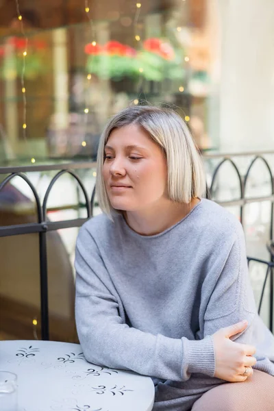 Nachdenkliche und lächelnde Frau sitzt am Tisch in Straßencafé — Stockfoto