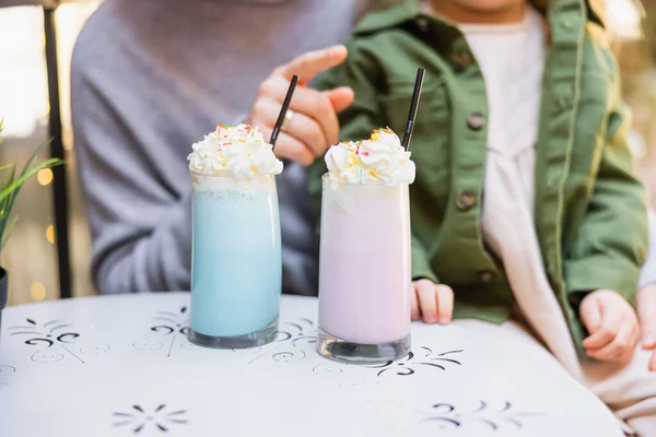 Vue recadrée de la femme pointant vers des lunettes avec milkshake près de la fille dans le café de la rue — Photo de stock